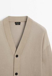 Beige gerippter Cardigan mit V-Ausschnitt, langen Ärmeln und drei schwarzen Knöpfen auf der Vorderseite. Strukturierter Strickstoff mit lockerer Passform.
