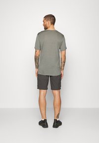 Szary t-shirt z krótkim rękawem, luźny krój, zestawiony z czarnymi szortami cargo z bocznymi kieszeniami. Model ma na sobie czarne buty sportowe.