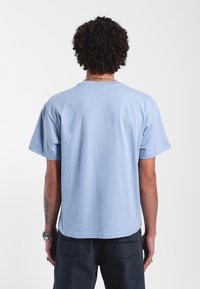 Camiseta de algodón de color azul claro con mangas cortas, cuello redondo y un ajuste relajado. La parte posterior presenta un acabado suave y texturizado.