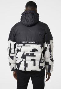 Chaqueta acolchada en blanco y negro con grandes letras gráficas. Cuenta con una capucha y la marca "Helly Hansen" en la parte trasera.