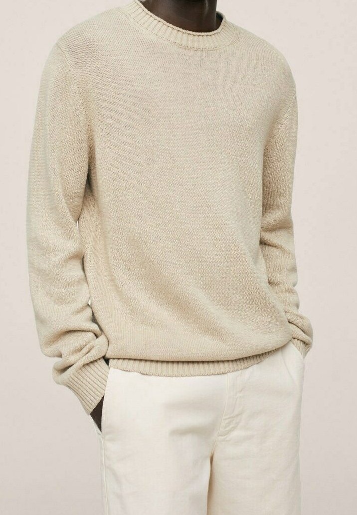 Beiger, gestrickter Pullover mit einem gerippten Rundhalsausschnitt und langen Ärmeln, ausgestattet mit einem strukturierten Stoff und einer lockeren Passform, kombiniert mit hellen Hosen.