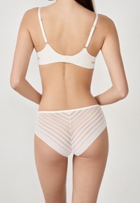 Hellbeige BH und passende hochgeschnittene Unterhose. Der BH verfügt über verstellbare Träger und eine glatte Oberfläche; die Unterhose hat ein gestreiftes Netzmuster.