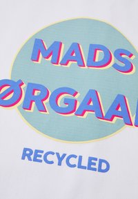 Tissu blanc avec un texte audacieux et coloré. Design circulaire avec "MADS ØRGAAN" en bleu et "RECYCLED" en bleu clair en dessous.