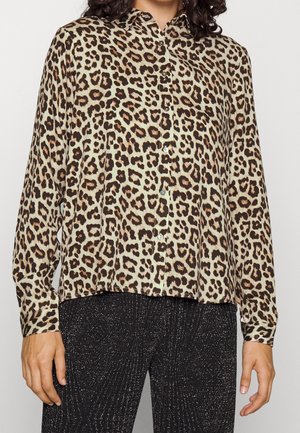 Woman wearing a long-sleeve leopard print button-up shirt and black glittery pants, standing with arms relaxed by sides.