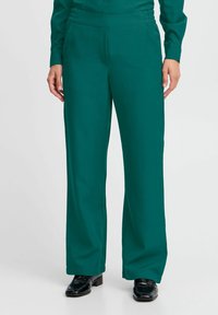 Pantaloni a gamba larga in tessuto liscio color teal con vita alta e tasche laterali. Abbinati a scarpe nere per un look curato.