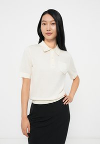 Valge lühikeste varrukatega polo-särk, millel on krae, eesmine tasku ja ribatud äär. Seljas must seelik, näidates lihtsat disaini.
