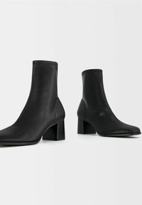 Czarne botki do kostki o gładkiej, skórzanej fakturze, z kwadratowym noskiem i szerokim obcasem, zaprojektowane tak, by dobrze przylegały do kostki.