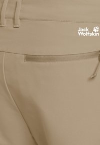 Pantaloni beige Jack Wolfskin in primo piano che mostrano una tasca posteriore con una striscia testurizzata e un piccolo dettaglio con cordino.