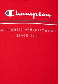 Tela roja con texto en blanco y negro: "Champion", "Authentic Athleticwear" y "Desde 1919" con dos líneas horizontales por encima del texto.