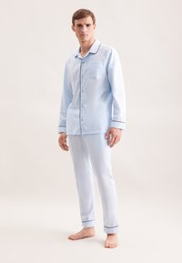 Ensemble de pyjama en coton bleu clair comprenant une chemise à boutons avec une poche poitrine, un passepoil contrasté bleu foncé et un pantalon ajusté assorti.
