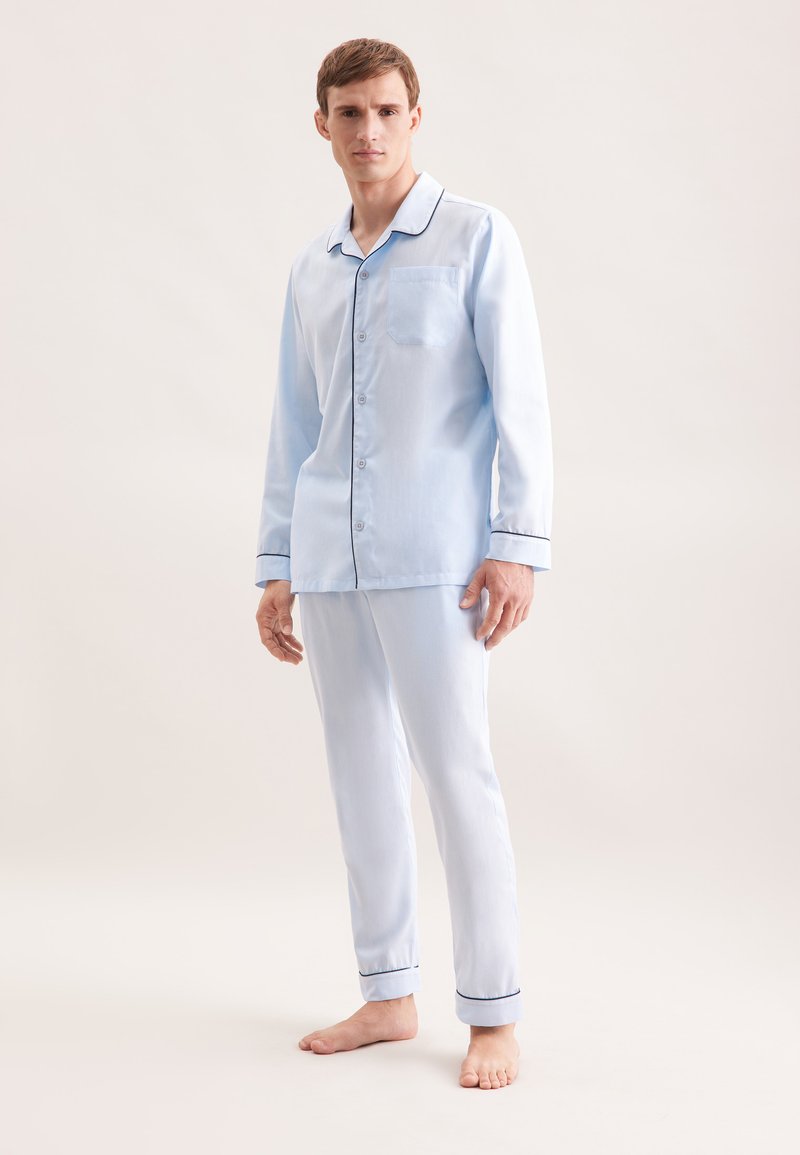 Ensemble de pyjama en coton bleu clair comprenant une chemise à boutons avec une poche poitrine, un passepoil contrasté bleu foncé et un pantalon ajusté assorti.