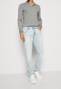 Jeans in denim azzurro chiaro con taglio dritto, abbinati a una maglietta a polo grigia a maniche lunghe. Sneakers bianche completano l'outfit.