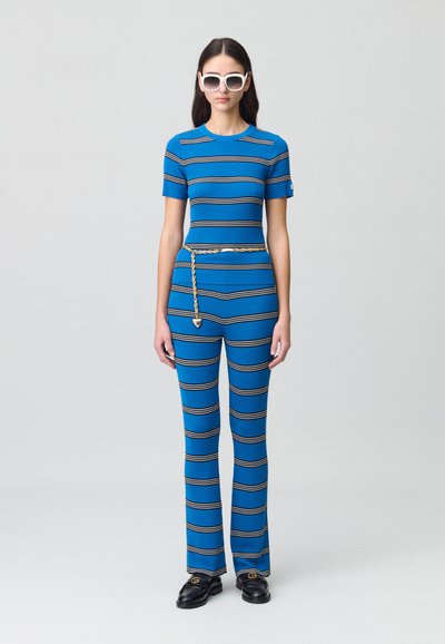 Completo due pezzi a righe blu realizzato in tessuto a costine; top a manica corta e pantaloni svasati; adornato con una cintura in catena dorata e scarpe nere.