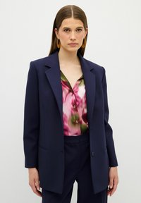 Námořnický blazer s upraveným střihem, dvěma předními kapsami, spárovaný s květinovou košilí s knoflíky v růžových a zelených odstínech. Hladká struktura látky.