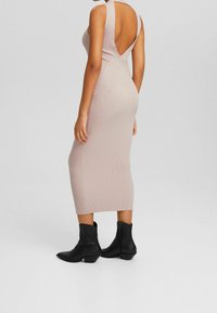 Robe midi à côtes de couleur rose pâle avec un dos en V profond. Accordée avec des bottines noires au bout pointu et à petit talon.