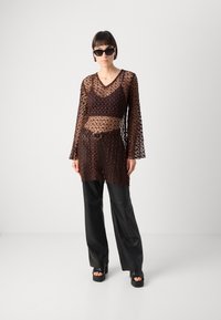 Sheer brown crochet top with a V-neck, long sleeves, layered over a dark top, paired with black leather wide-leg pants and platform heels.