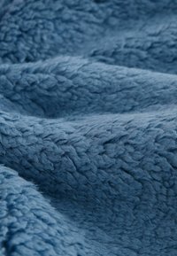Gros plan sur un tissu en polaire bleu doux et texturé, avec des fibres visibles et de légers plis créant une surface douillette et confortable.
