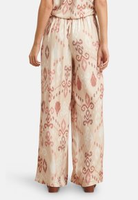 Flowy, lightweight, patterned pants with a beige base, featuring red and white designs. Elastic waistband and wide legs.