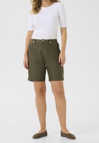 Krótkie spodenki w oliwkowej zieleni z dwoma przednimi kieszeniami, dopasowanym krojem i złotymi guzikami jako akcentami. Połączone z dopasowanym białym topem.