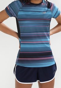 Camiseta deportiva de manga corta con rayas horizontales azules y rosas, fabricada con material sintético y detalles laterales negros; combinada con pantalones cortos azul marino.
