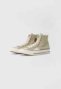 Helle grüne Canvas High-Top-Sneaker mit weißen Schnürsenkeln, Gummizehenschutz und kontrastierender weißer Sohle mit zwei schwarzen Streifen.