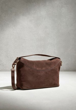 Hnedá semišová kabelka cez rameno s krátkou rukoväťou a odnímateľným remienkom, na neutrálno šedom pozadí s jemným osvetlením.