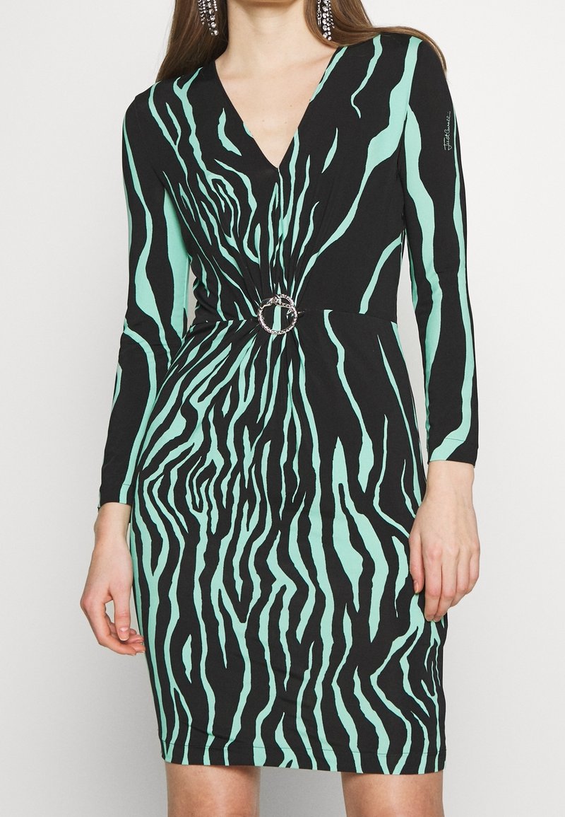 Robe à manches longues avec col en V, rayures zébrées noires et vert menthe, cintrée à la taille avec une boucle circulaire argentée.
