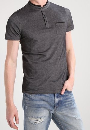 Polo à manches courtes gris foncé avec un col à bouton-pression, doté d'une poche poitrine et d'un tissu doux, associé à un jean clair déchiré.