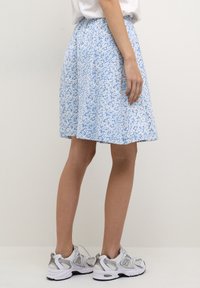 Vaaleansininen hame, jossa on valkoinen kukkakuosi, kuminauhavyötärö, polvipituinen, tehty pehmeästä kankaasta. Yhdistetty valkoisiin urheilutennareihin.