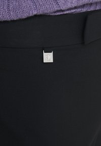 Svarta byxor i tyg med en silverfärgad "RLL"-logotyp på midjan, i kombination med en texturerad lila stickad tröja som visas ovan.