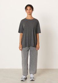 Sivo kratka majica z rahlim krojem, kombinirana s svetlo sivimi širokimi kavbojkami. Model nosi sive atletske čevlje z minimalističnim dizajnom.