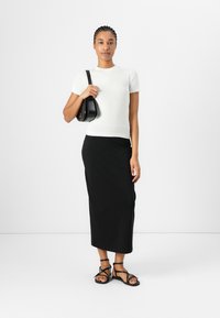 Hvid ribbet T-shirt med korte ærmer, sort ankellang nederdel og sorte sandaler med remme. Model holder en sort, rund håndtaske.