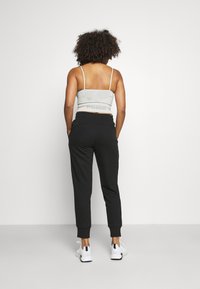 Top corto gris con tirantes finos y logo en la parte de atrás, combinado con pantalones jogger negros ajustados y zapatillas deportivas blancas.