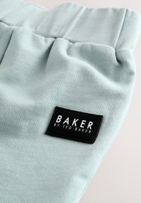 Pantalon de jogging bleu clair à la texture douce, avec un patch logo rectangulaire noir portant l'inscription "BAKER BY TED BAKER."