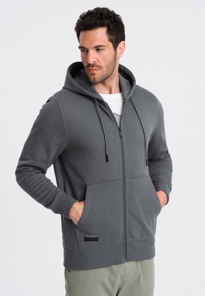 Grijze zip-up hoodie met een trekkoordcapuchon, voorzakken, geribbelde manchetten en een subtiele logodetail op de zoom. Zachte stoftextuur.