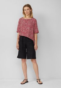 Rood gemusterde blouse met korte mouwen, gecombineerd met zwarte linnen shorts. De blouse heeft een losse pasvorm en een zijstrikdetail.