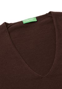 Hnědý svetr s výstřihem do V vyrobený z měkké pleteniny. Na výstřihu se nachází zelená visačka značky "UNITE COLORS OF BENETTON".