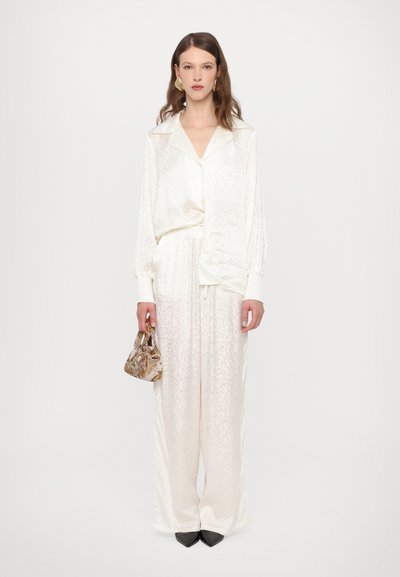 White textured two-piece outfit featuring a button-up shirt with a collar and wide-leg pants. Paired with a small patterned handbag.