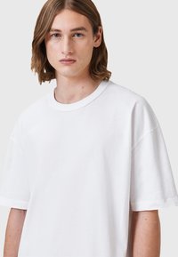 T-shirt bianca in cotone oversize con collo a giro e maniche corte. Tessuto morbido, vestibilità rilassata, design minimale, adatta per un abbigliamento casual.