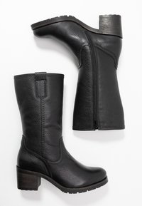 Botas de tobillo de cuero negro con un acabado texturizado, puntera redondeada, cremallera lateral y tacón de madera ancho. Suela de goma antideslizante.
