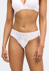 Balti mežģīņu apakšveļa ar ziedu rakstiem, ar viļņotu malu, gludu tekstūru un zemu jostas līniju.