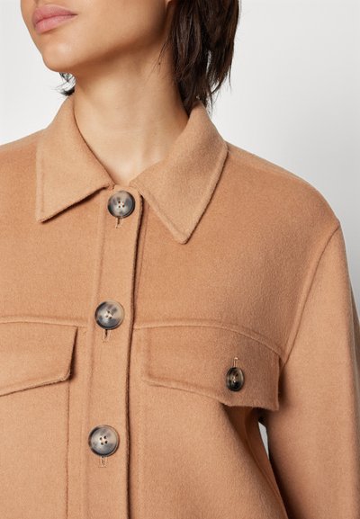 Beige Wollhemdjacke mit strukturiertem Kragen und zwei vorderen Taschen. Verfügt über große, dunkle Knöpfe und einen weichen, strukturierten Stoff.