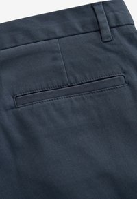 Navyblauwe stoffen broek met een gladde textuur, voorzien van een achterste weltzak en gestikte details langs de rand van de zakken.