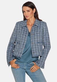 Blauwe tweed cropped jasje met rafelige zoom, opvallende knopen en een kraag, gecombineerd met een satijnen top en casual jeans.