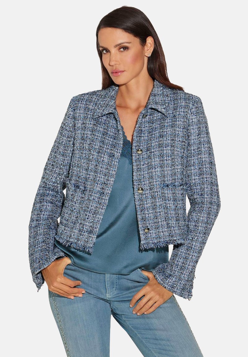 Blauwe tweed cropped jasje met rafelige zoom, opvallende knopen en een kraag, gecombineerd met een satijnen top en casual jeans.