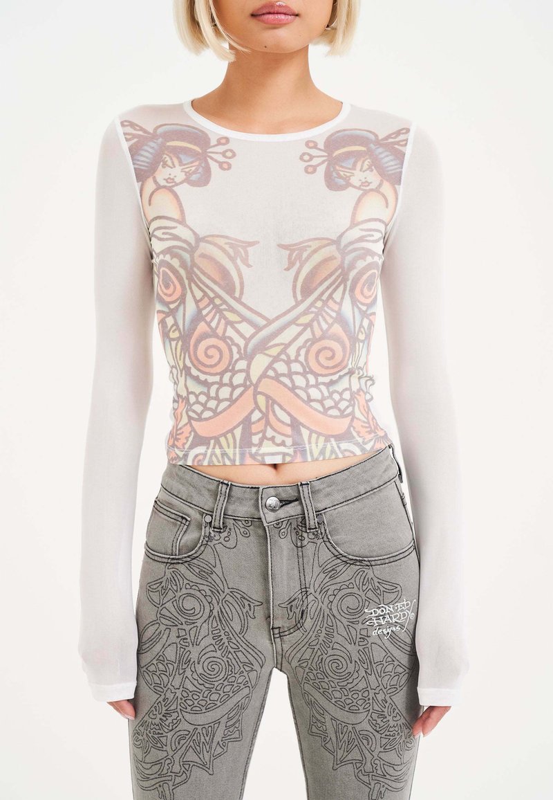 Blusa a maniche lunghe trasparente con una grafica stampata colorata. Abbinata a jeans grigi con disegni intricati e testo ricamato bianco.