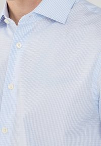 Chemise à carreaux bleu clair, en coton doux, avec col structuré, ourlet arrondi et boutons blancs sur la patte de boutonnage frontale.