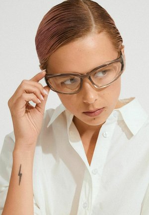 Transparent brown safety glasses with a sleek, wraparound design, worn with a white button-up shirt, showcasing clear lenses and a smooth texture.