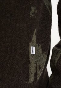 Dunkelbrauner Strickpullover mit grünem Camouflage-Muster. Verfügt über ein Stofflabel mit dem aufgenähten Text "Rastafaris" an der Seite. Weiche Textur.