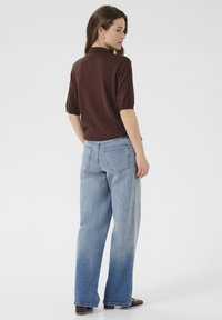 Polo shirt corto marrone a maniche corte abbinato a jeans a vita alta blu chiaro con gamba larga, dotato di tasche posteriori e sfumatura di colore graduale.